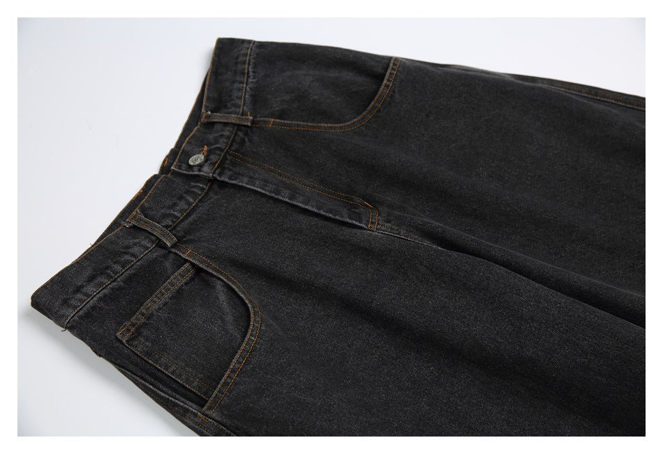 Close-up of black denim jeans showing the buttoned waistband, front pocket, and contrast stitching.