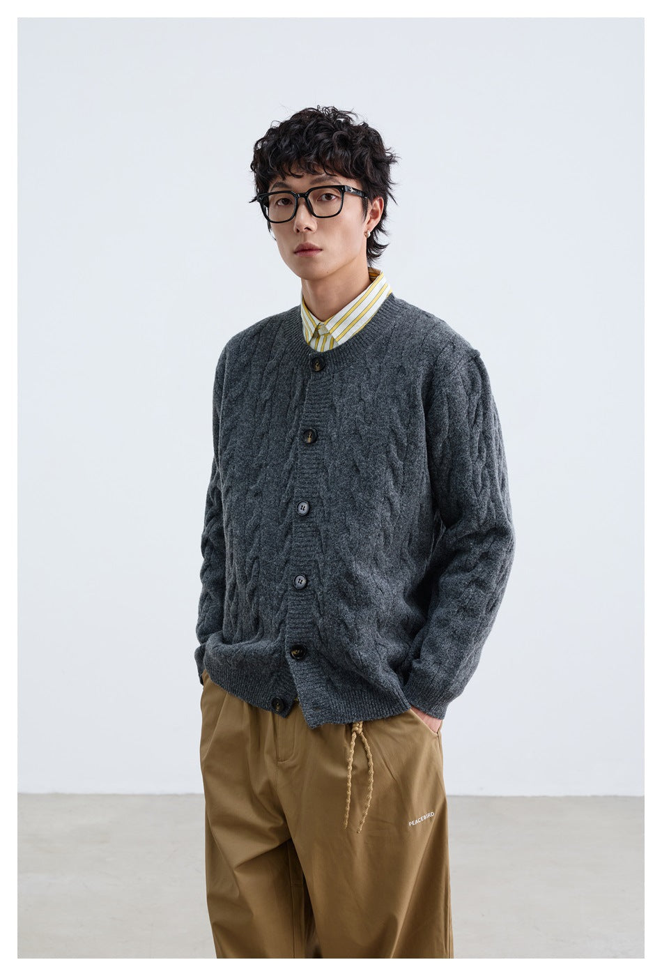 Front view of a model wearing a charcoal cable-knit button cardigan over a yellow-striped shirt.