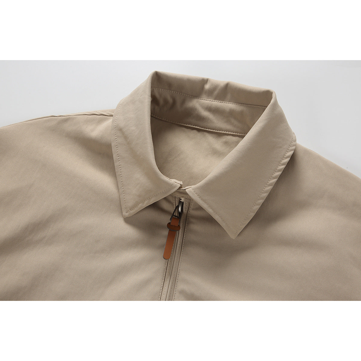 Close-up of a beige jacket's pointed collar and front zipper with a brown pull tab.