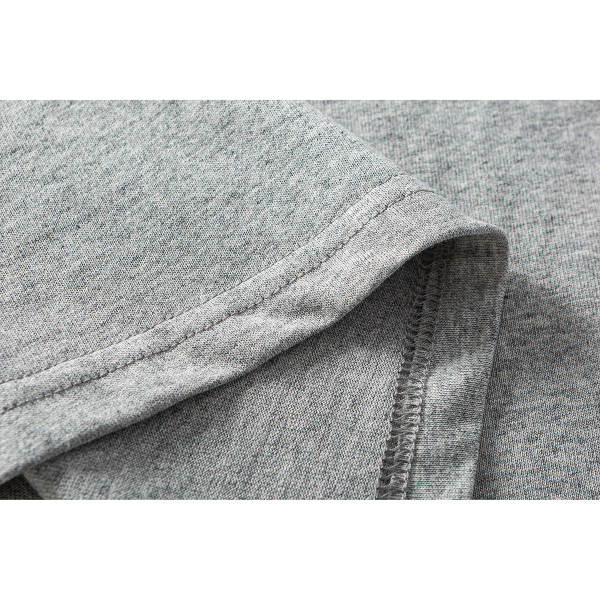 Close-up of gray heather T-shirt fabric showing a folded, double-stitched hem and overlocked seam.