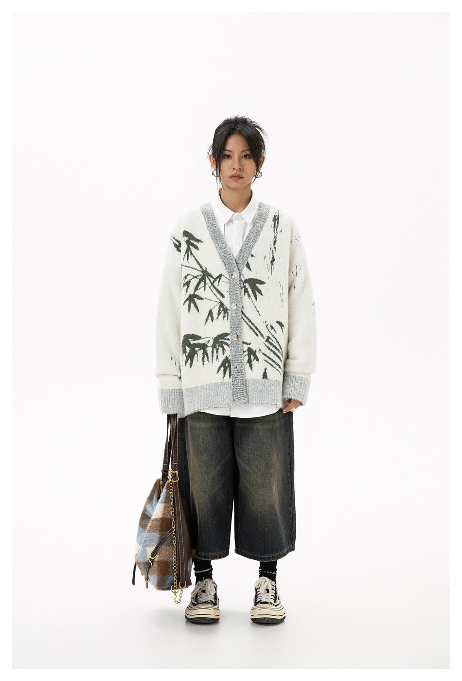 Model wearing beige bamboo-pattern cardigan over a white shirt, carrying a plaid tote bag, with denim shorts