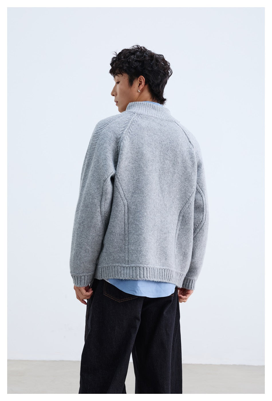 Back view of a model wearing a light gray knit cardigan with raglan sleeves and ribbed side panels.