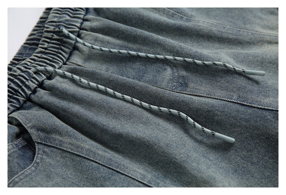 Faded blue denim pants detail showing two gray drawstrings, the elastic waistband, and a pocket seam.