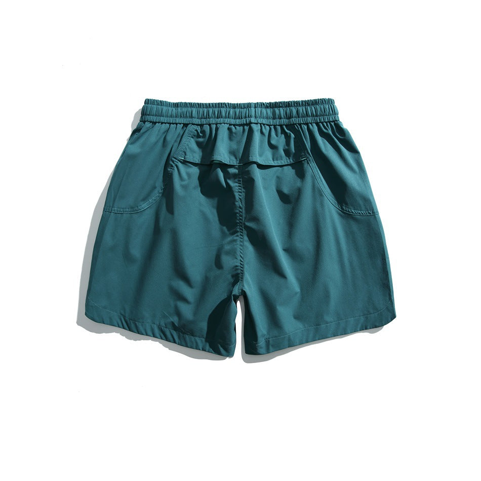 Teal athletic shorts shown from the back, with an elastic waistband, flap pocket, and curved side pockets.