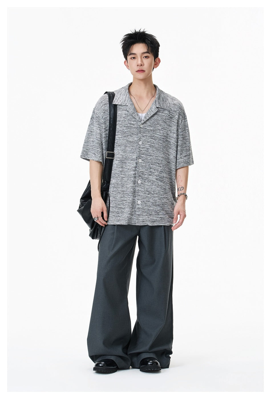Model wearing a light gray heathered short-sleeve camp-collar shirt with wide dark gray trousers and a black shoulder bag