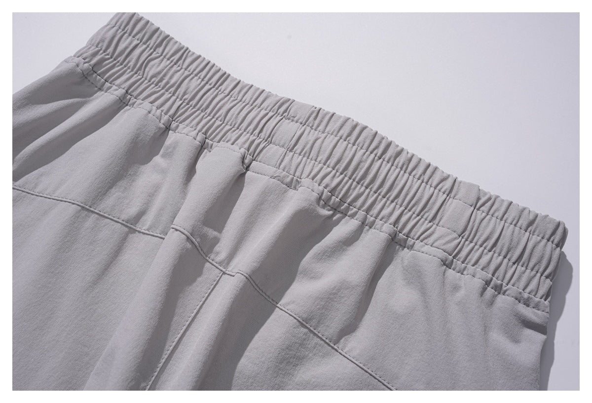 Close-up of light gray trousers showing the gathered elastic waistband and stitched front panels.