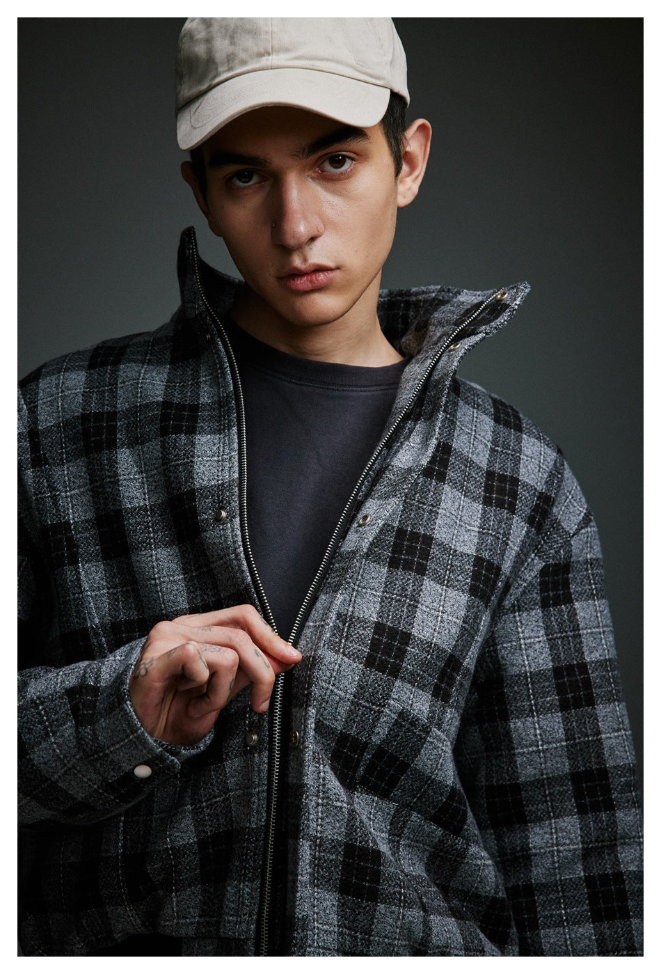 Close-up of a man wearing a gray and black plaid zip-front jacket open over a dark shirt.