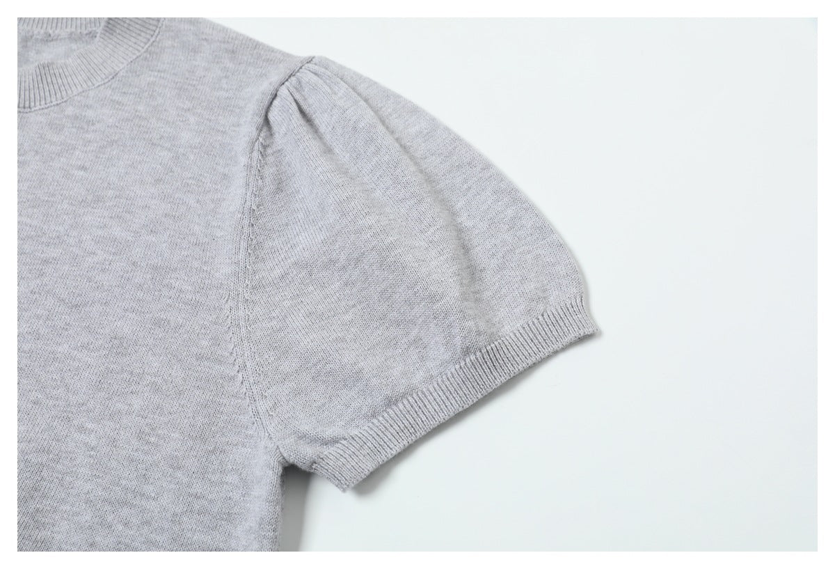 Close-up of a light gray sweater's short sleeve, shoulder seam, and ribbed sleeve hem.
