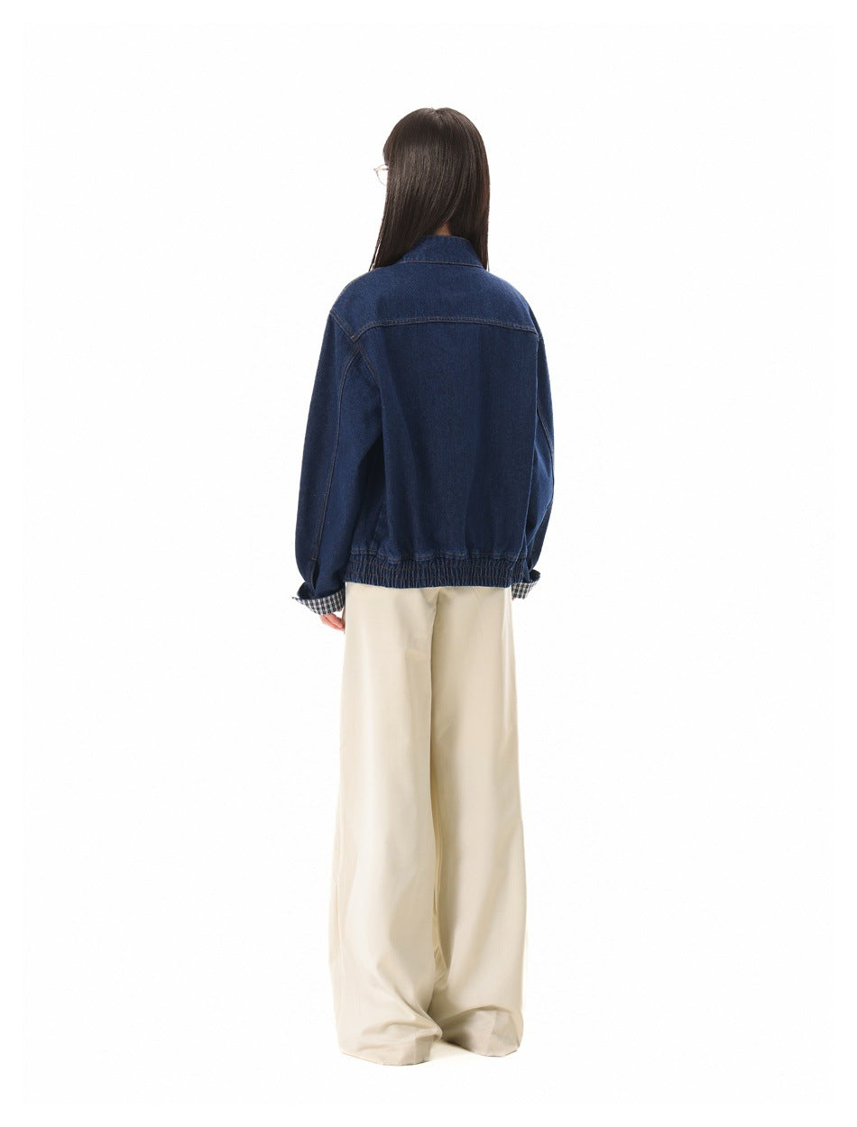 Rear view of a person wearing a dark indigo denim jacket with checked cuffs and wide cream trousers.