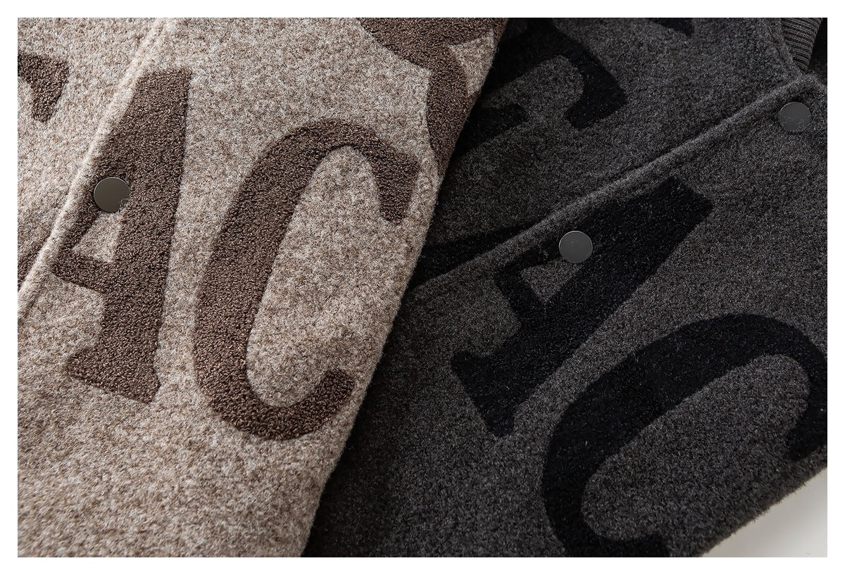 Close-up of beige and charcoal knit garments with oversized dark lettering and snap buttons.
