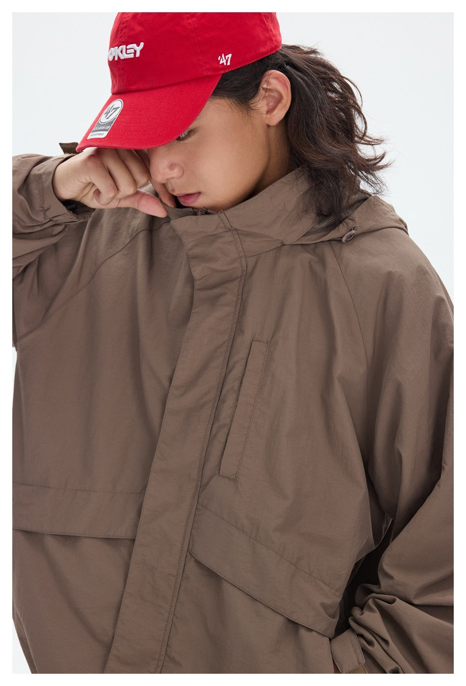 Close-up of a taupe jacket's high collar, hood, covered front closure and chest pocket on a model.