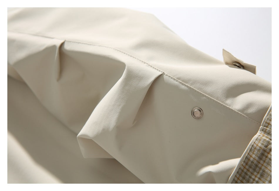 Close-up of a cream garment with a round metal snap fastener and folded seam.