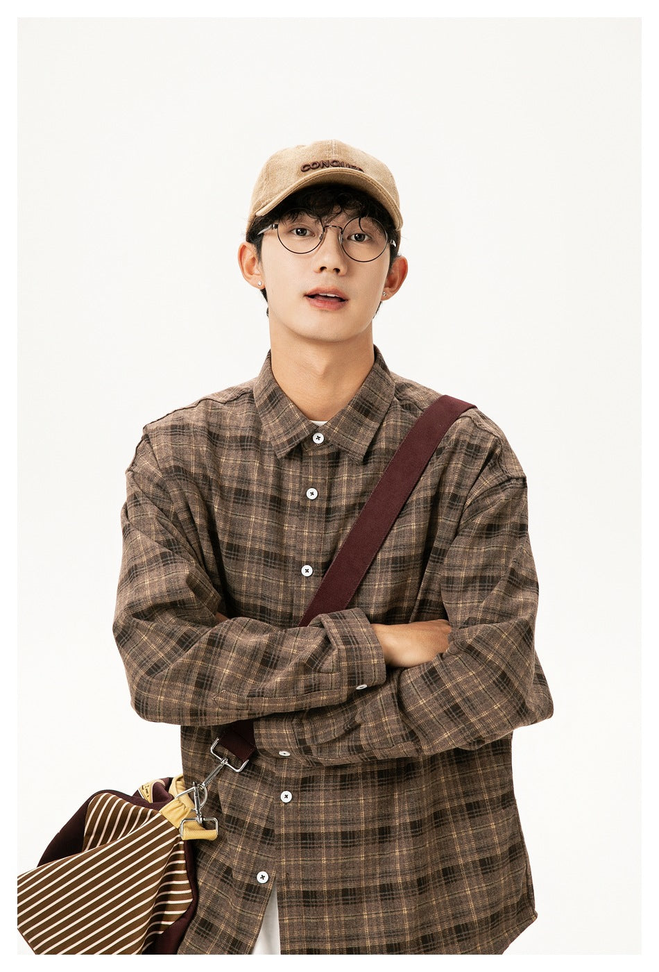 Close view of a model wearing a brown plaid button-up shirt, with a crossbody bag strap over the shirt.