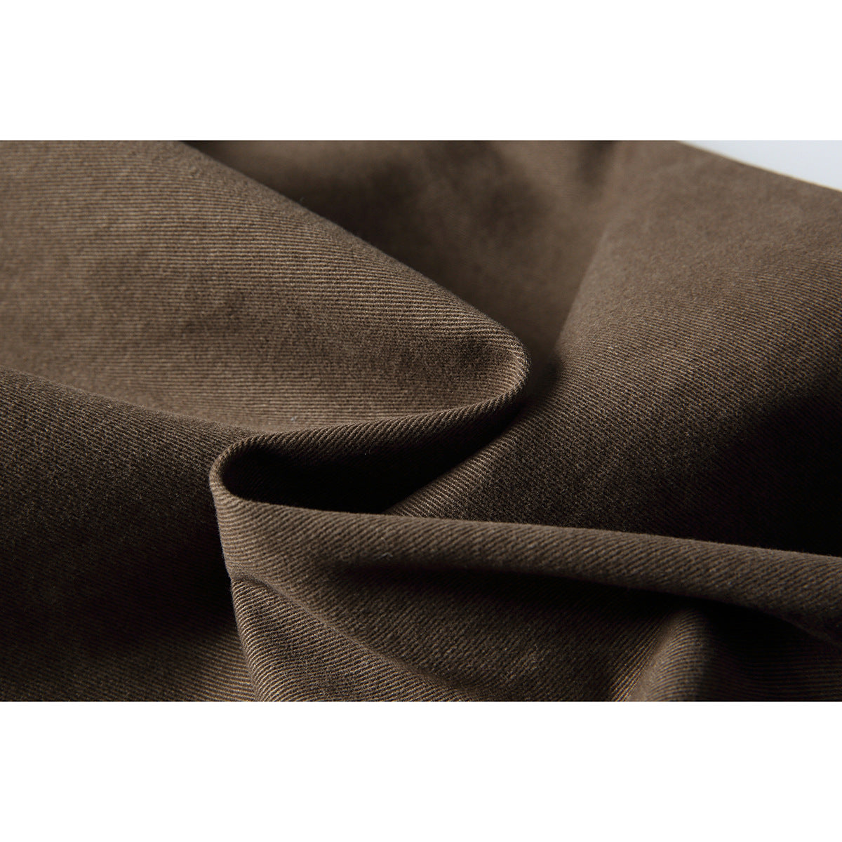 Macro view of brown trouser fabric showing its fine diagonal texture and drape.