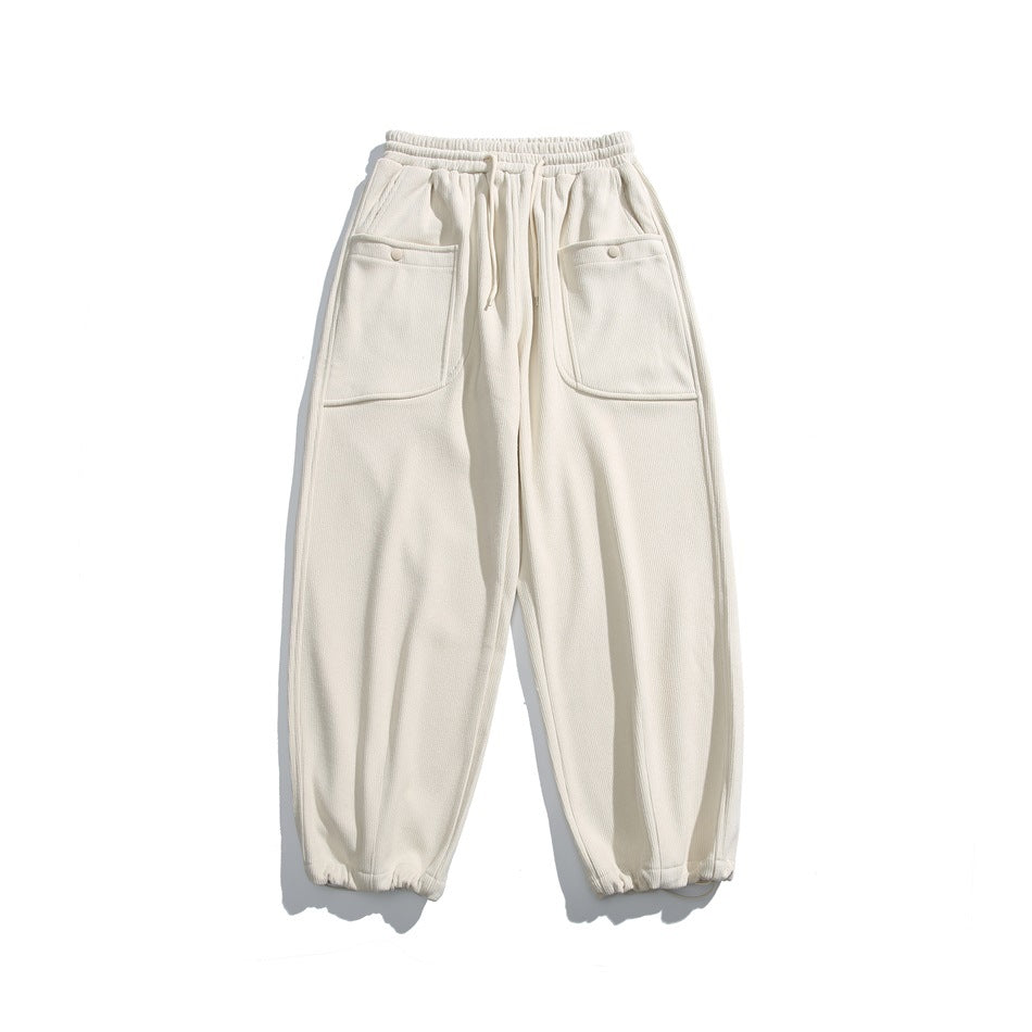 Front view of cream jogger pants with an elastic drawstring waist, large buttoned patch pockets, and elastic cuffs.