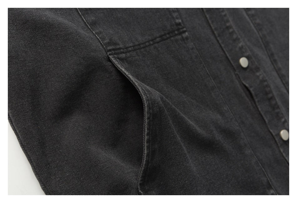 Close-up of a black denim garment showing stitched panels and silver snap buttons.