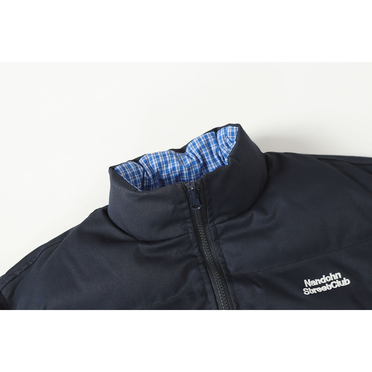 Close-up of a dark navy jacket collar with blue plaid lining, front zipper, and white chest embroidery.