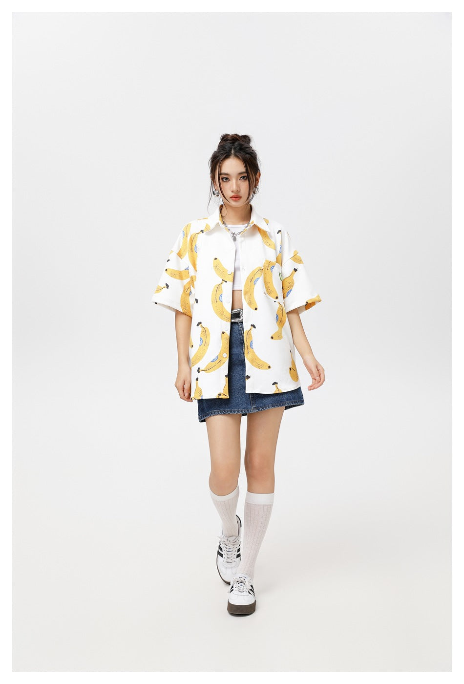 Full-length view of a model in a white banana-print short-sleeve shirt, denim mini skirt, knee socks and sneakers