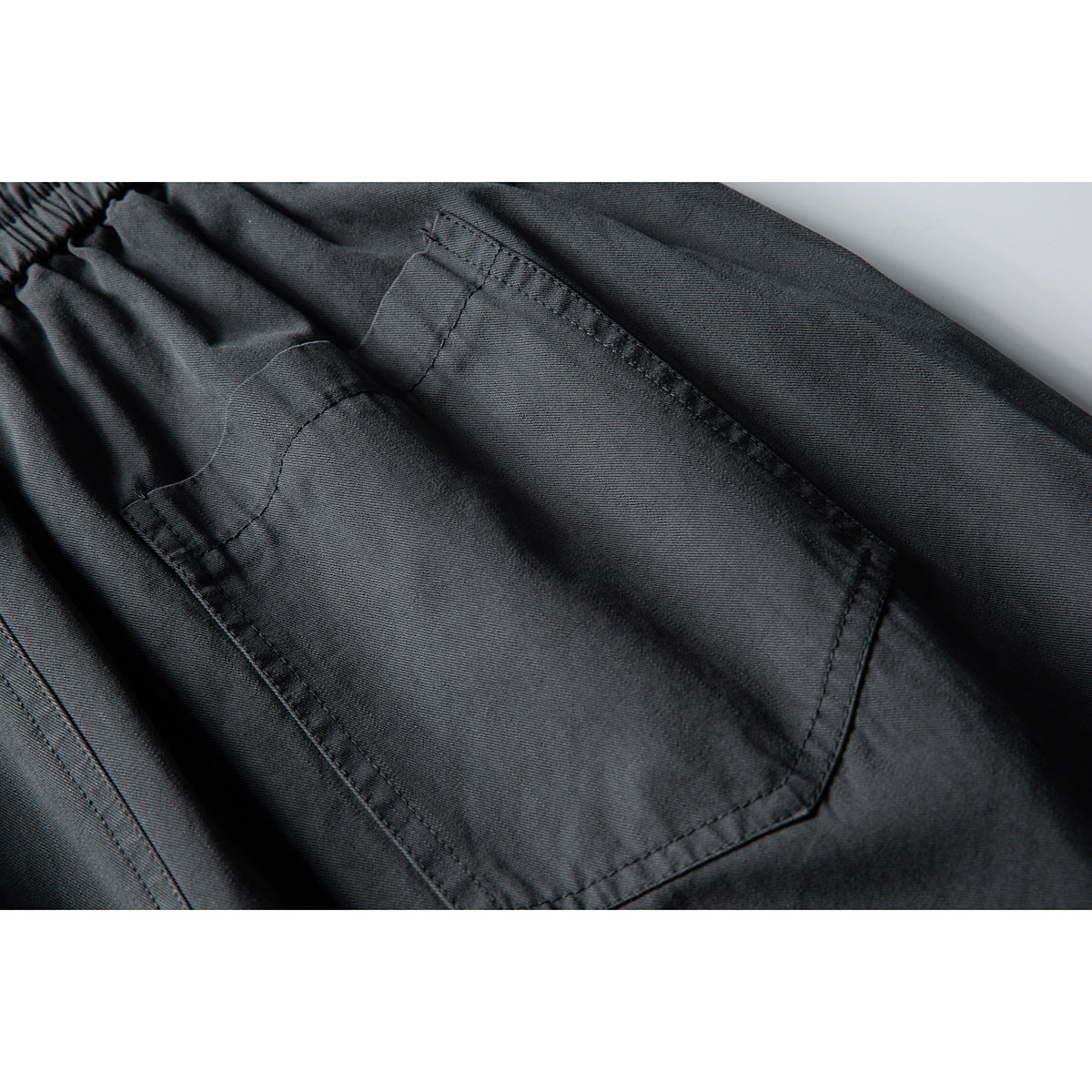 Close-up of a stitched patch pocket on charcoal pants, with part of the elastic waistband visible.