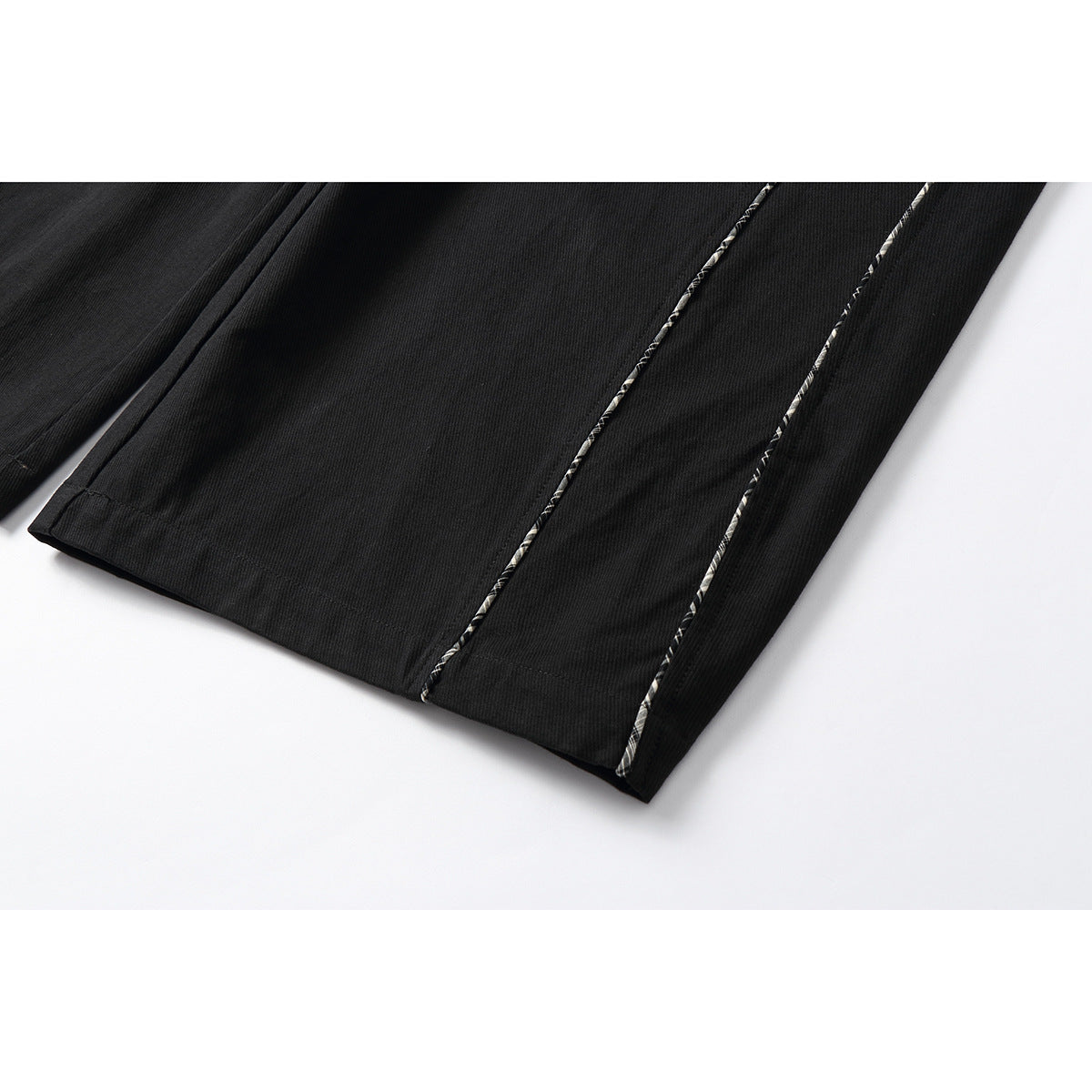 Close-up of black trouser hems with narrow black-and-white plaid piping along the legs.