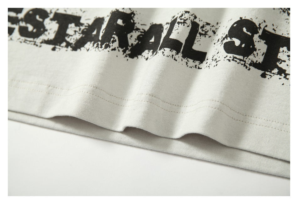 Close-up of an off-white shirt hem with stitching and part of a distressed black graphic.