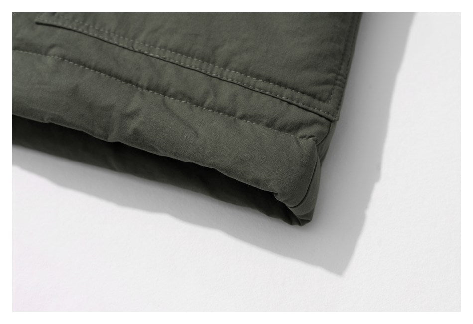 Close-up of a dark olive garment hem showing folded edges and parallel stitching.