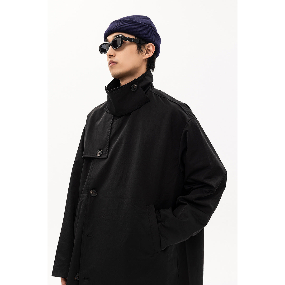Close view of a model wearing a black coat with a high collar, buttoned storm flap and roomy sleeves.