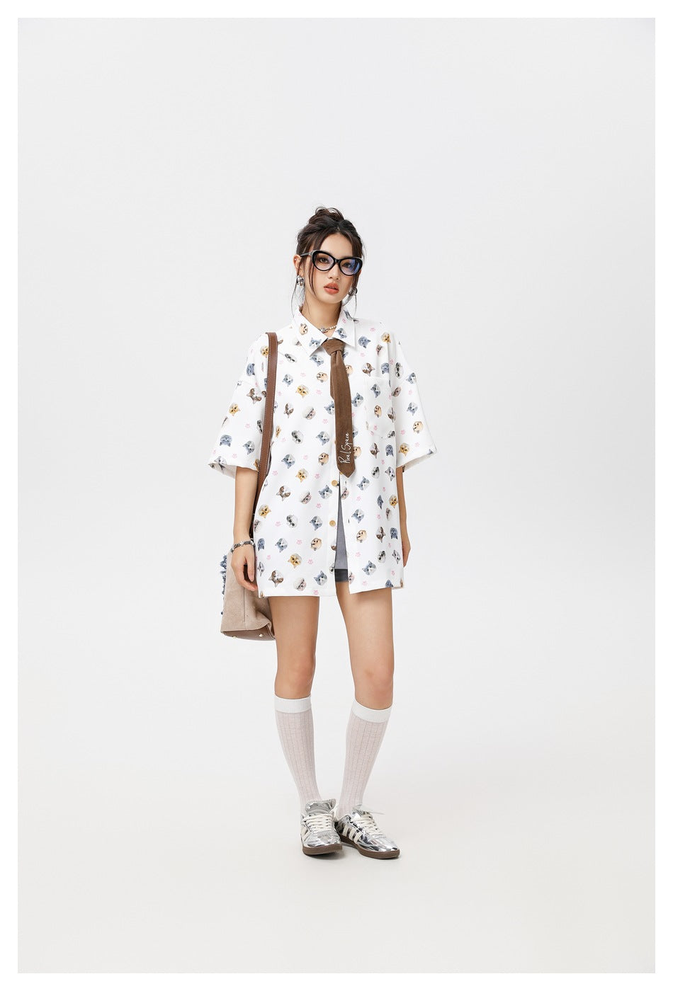 Full-length model wearing a white oversized cat-print shirt with a brown tie, knee socks and metallic sneakers.