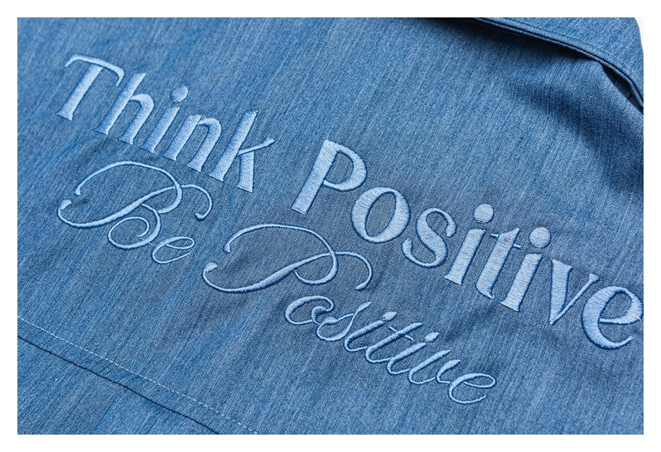 Close-up of blue denim embroidered with the words “Think Positive Be Positive” in light-colored thread.