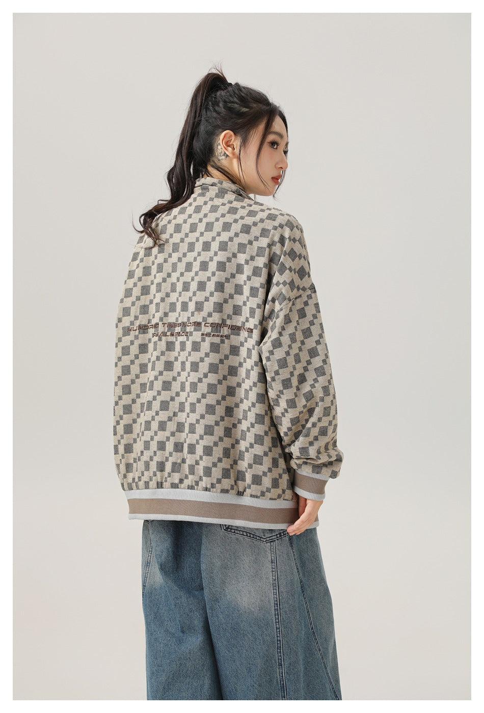Model wearing a beige and charcoal checker-pattern jacket with striped ribbed hems and small text across the back.