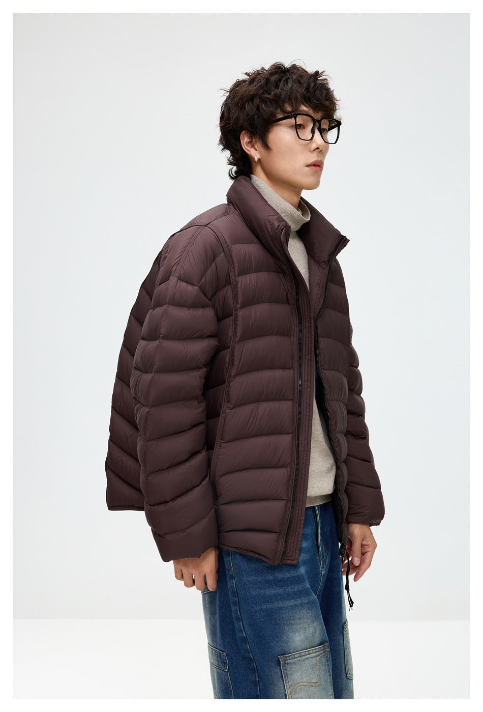 Angled view of a model wearing a dark plum-brown quilted puffer jacket with a high collar.