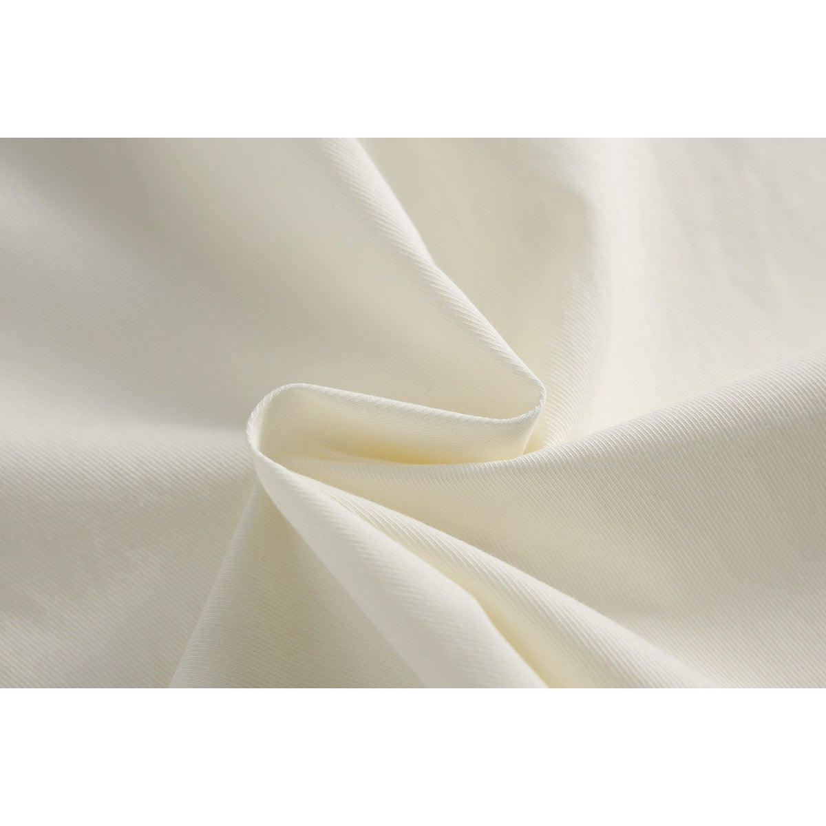 Close-up of ivory fabric arranged in soft folds, showing its fine diagonal weave.