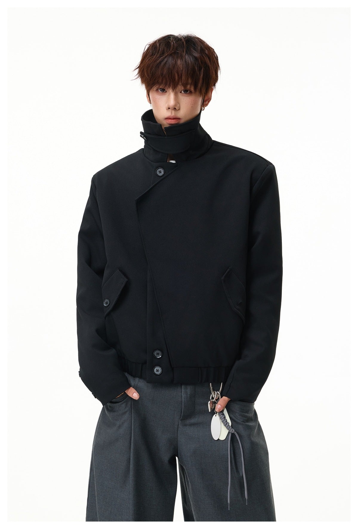 Model wearing a black jacket with the tall collar fastened, angled front closure, and buttoned pockets.