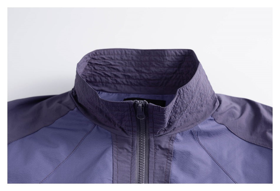 Close-up of a blue-violet jacket's high collar, dark contrast panels, stitching, and front zipper.