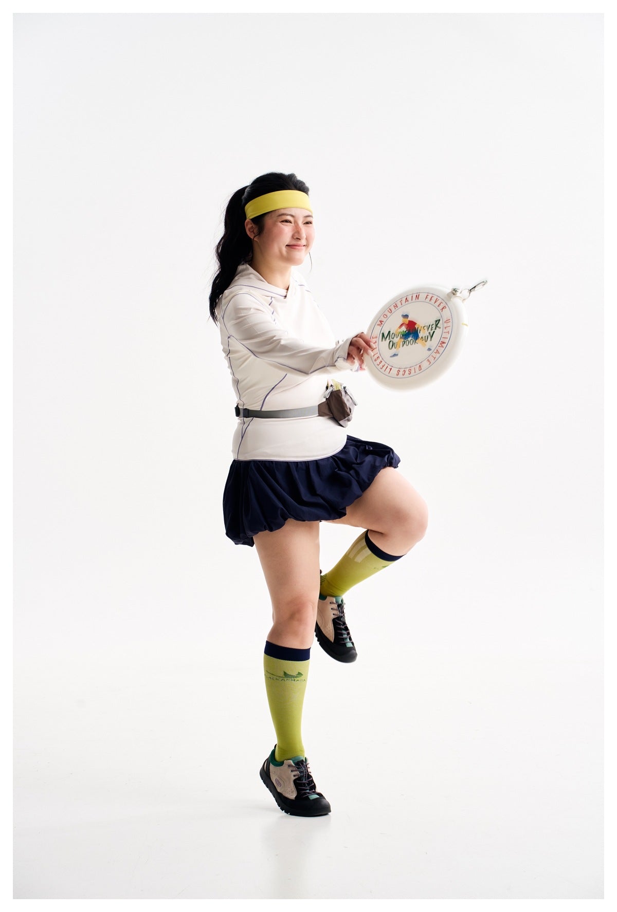 Model in an ivory top with purple piping and a navy bubble-hem skirt, holding a printed round disc.