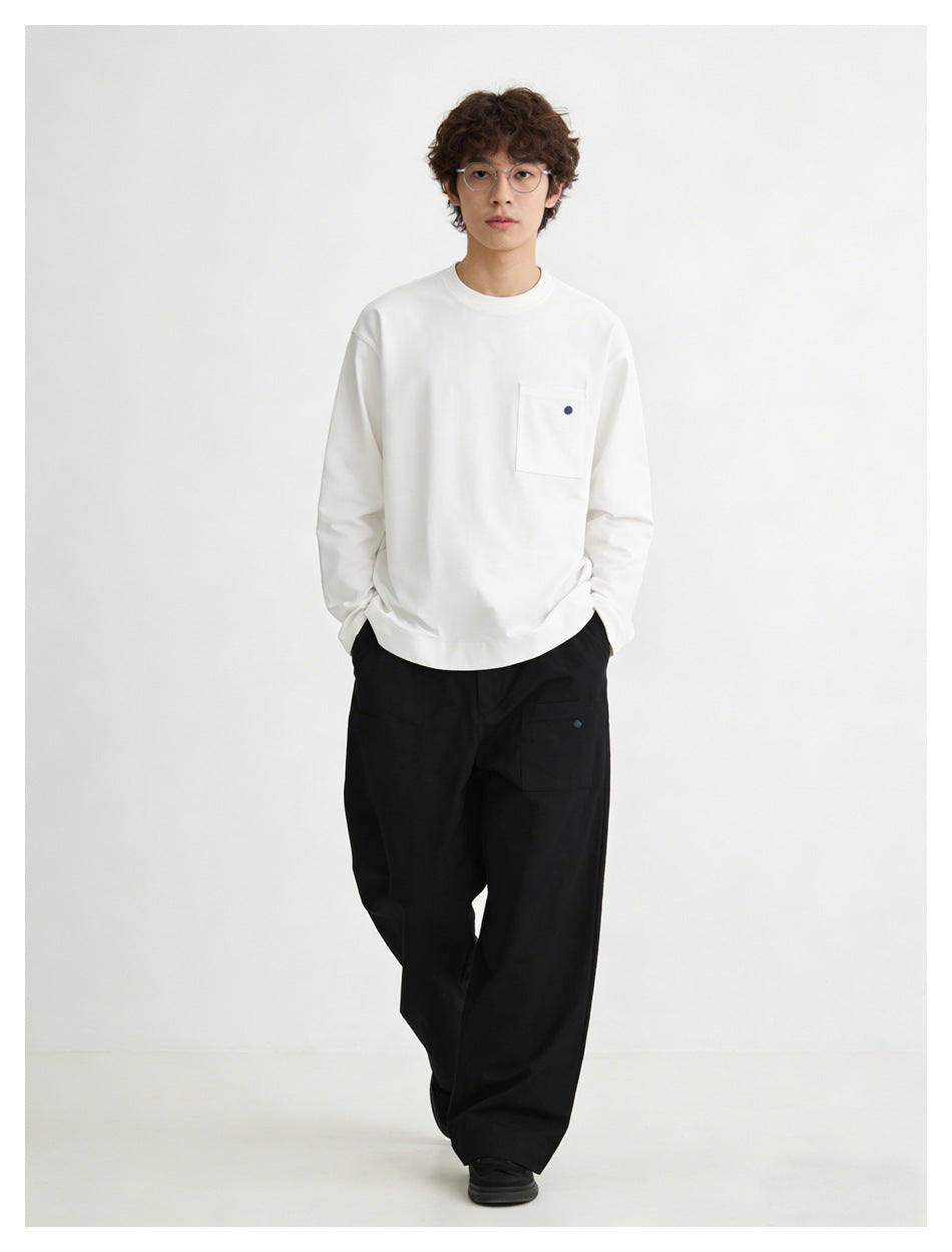 Model wearing a white long-sleeve crewneck top with a chest pocket and loose black trousers.