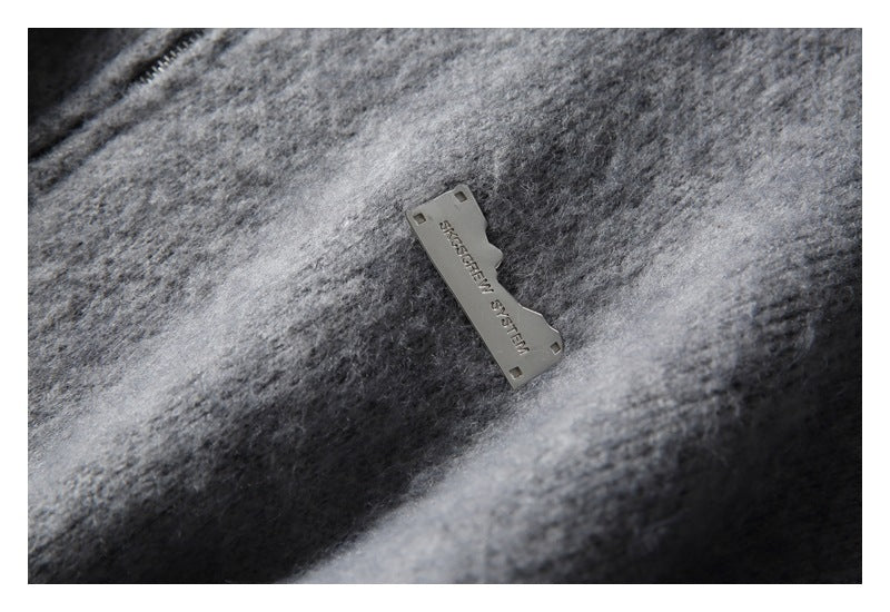 Close-up of a small engraved metal tag on mottled gray fuzzy knit fabric.