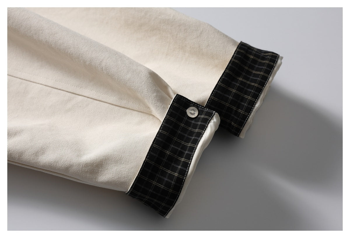 Ivory jacket sleeve with a wide black plaid cuff tab and a metal snap.