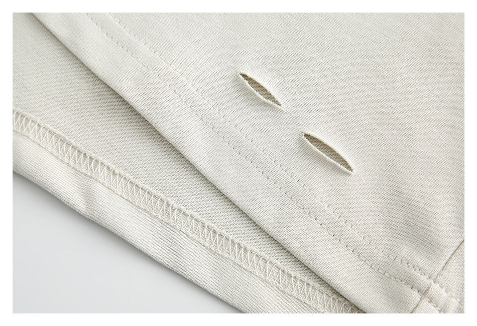Close-up of two slits and overlocked stitching along the hem of an ivory garment.