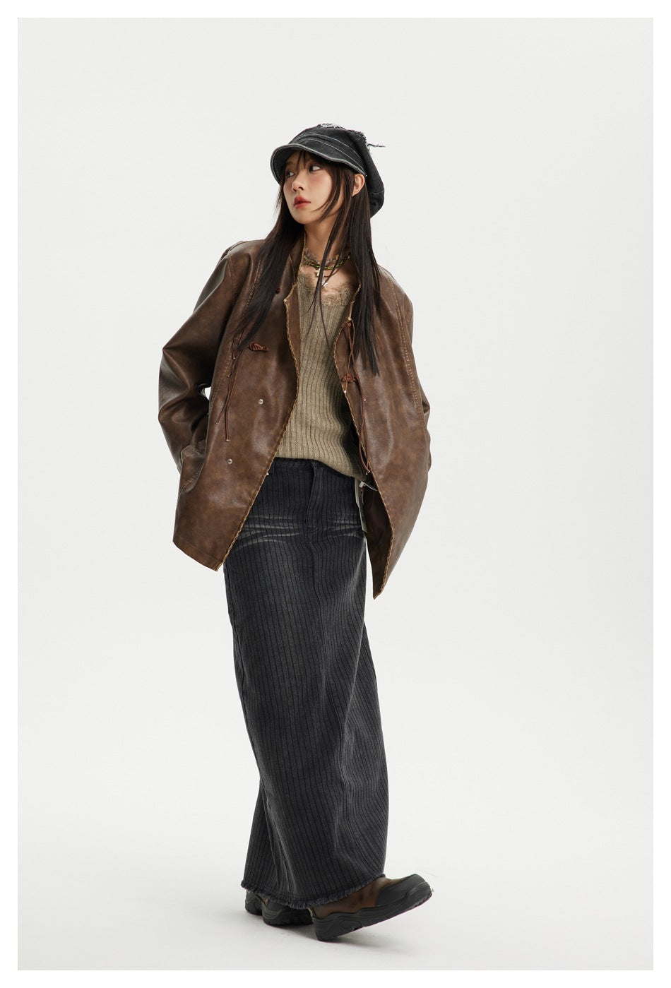 Full-length view of a model wearing an open brown jacket over a knit top and long dark skirt.