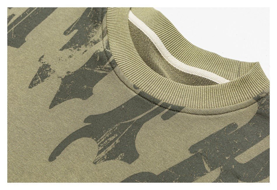 Close-up of an olive sweatshirt's ribbed crewneck and dark abstract camouflage-style print.
