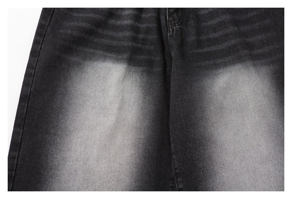 Close-up showing the faded gray wash and diagonal denim texture on charcoal-black shorts.