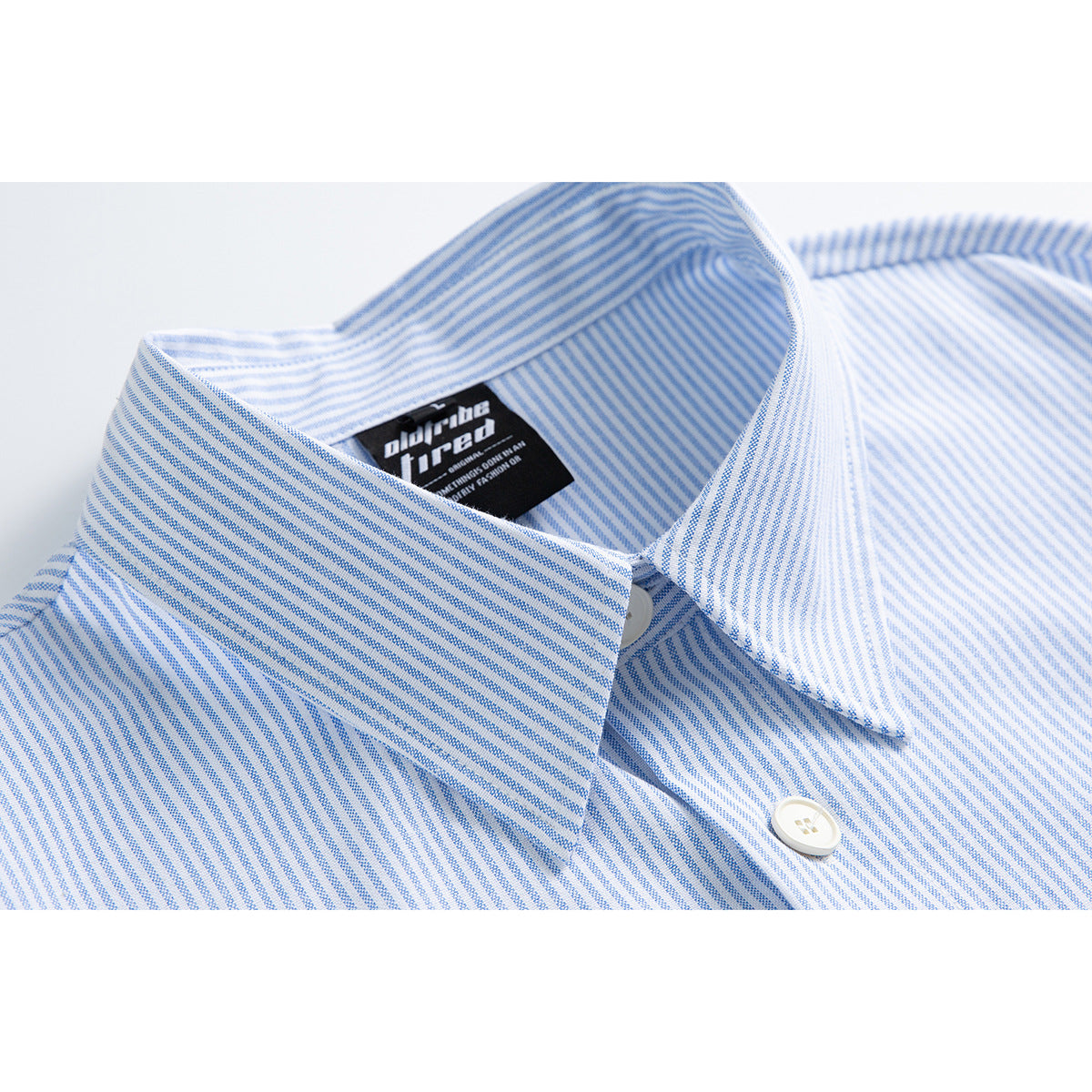 Close-up of a blue-and-white pinstriped shirt collar, button, and black neck label.