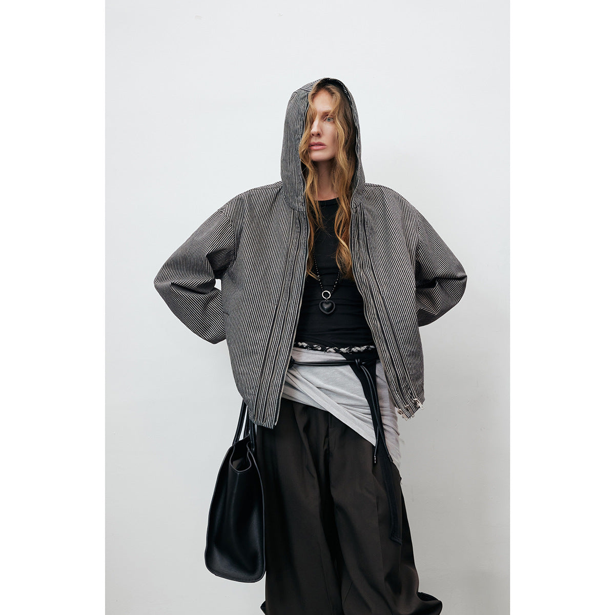 Model wearing a black-and-white pinstriped hooded jacket over dark trousers, with the jacket open.