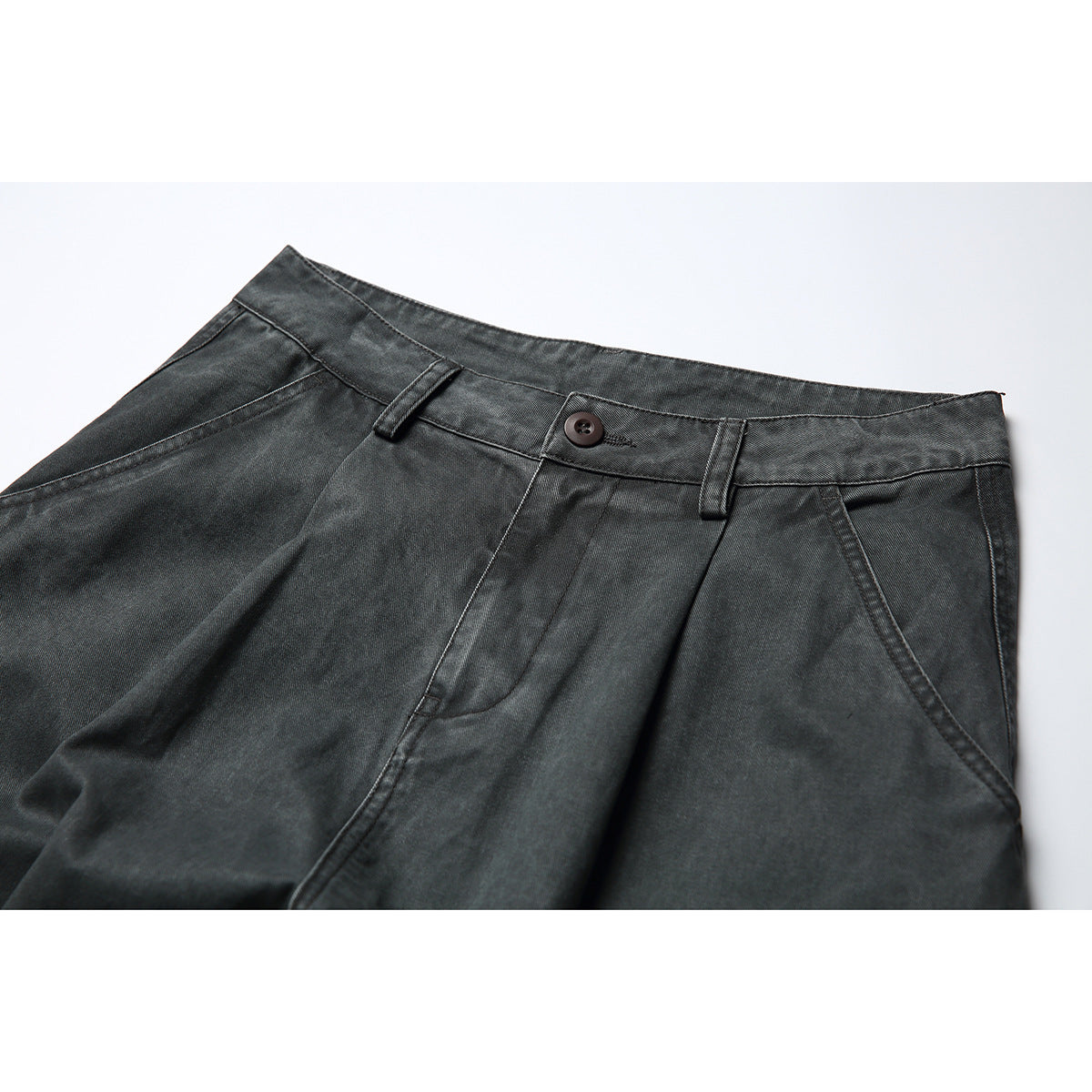 Close-up of charcoal gray cargo pants showing the waistband, button, belt loops, pleats, and angled pockets.