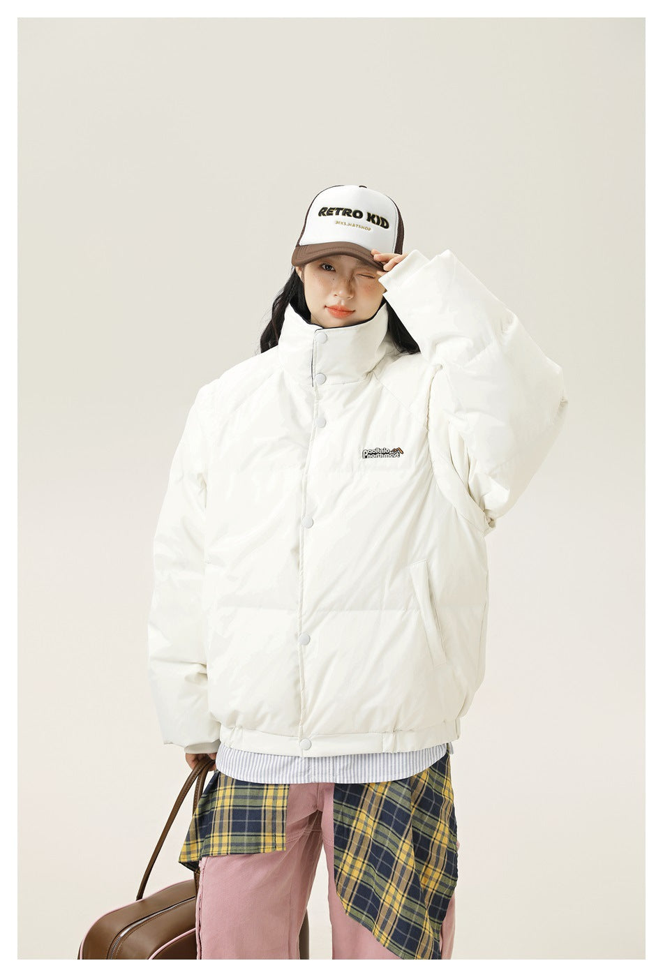 Closer front view of a model wearing an ivory snap-front puffer jacket with a high collar and side pockets.
