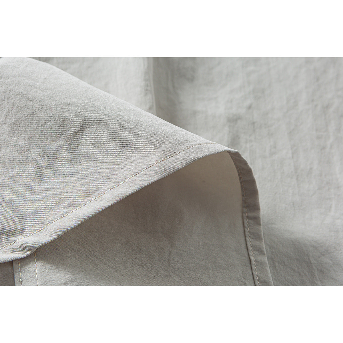 Close-up of the light beige overshirt's curved sleeve edge and stitched seams.