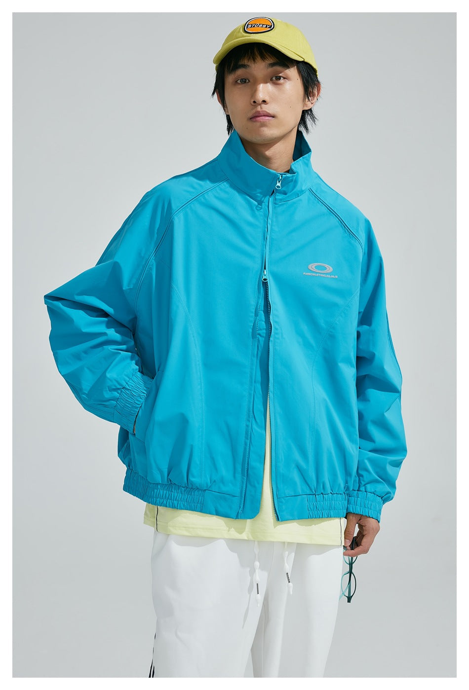 Front view of a model wearing a turquoise zip jacket with elastic cuffs and hem.