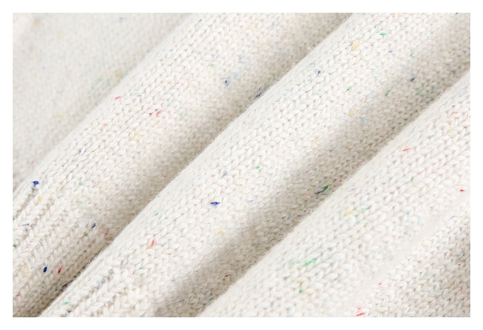 Close-up of off-white knitted fabric with scattered tiny multicolored flecks and raised folds.
