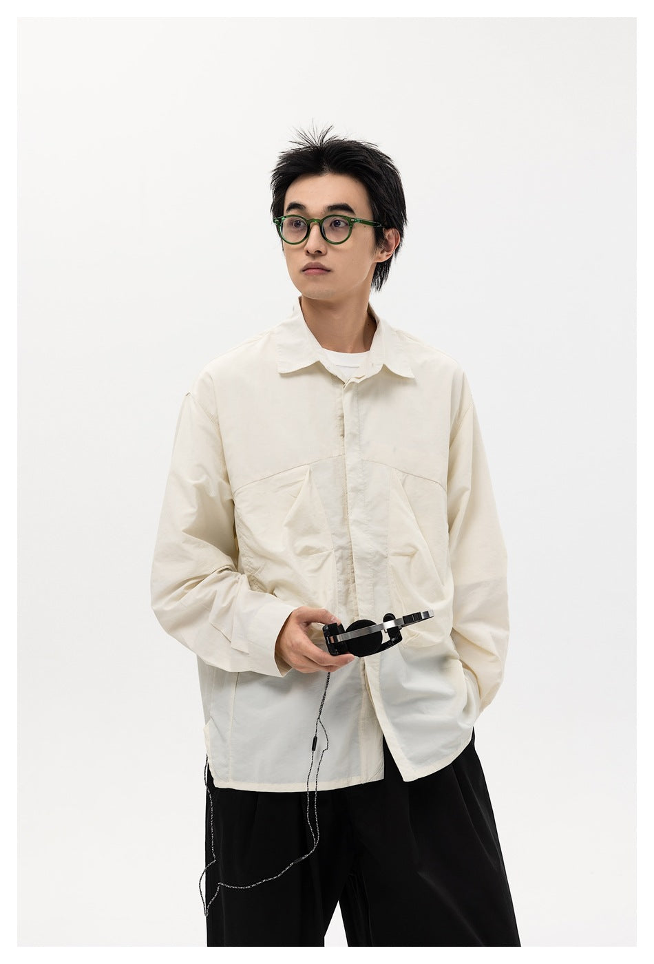 Model wearing an oversized ivory button-up shirt with large front pockets and black trousers.